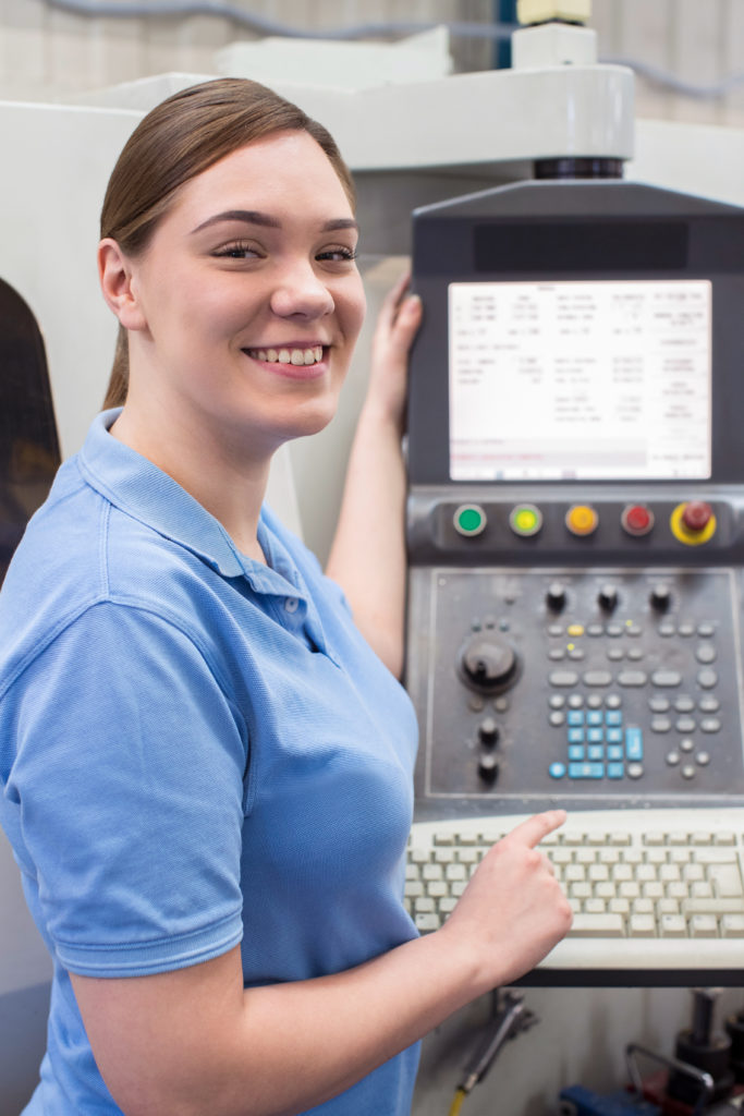 A female apprentice machinist operating a CNC machine in a factory